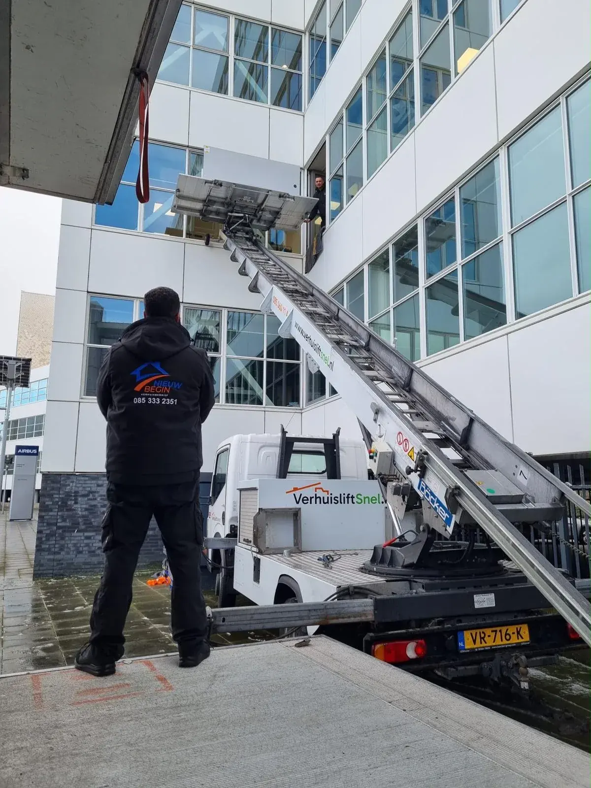 Verhuizer bij de verhuislift tegen een kantoorpand met glazen gevel